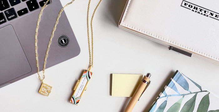 A laptop, fortune & frame box, notebook, pen, and sticky notes all together next to a Secret Diary Book Locket (Pearl) and Deco Fortune Locket (Multi Color) with a fortune that reads